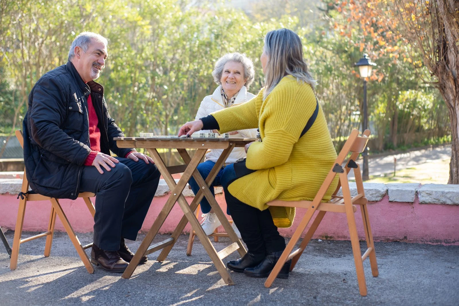 Older adults smiling and playing dominoes together at an outdoor table